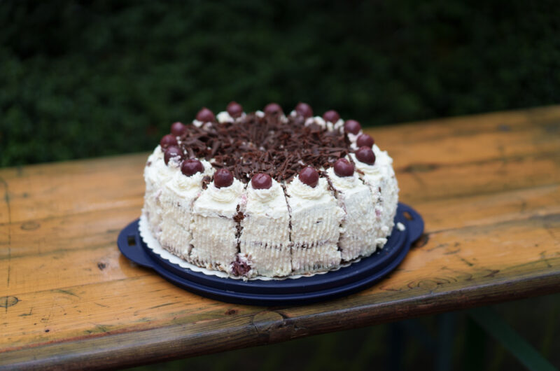 Eine Schwarzwälder Kirschtorte auf einer blauen Kuchenteller und einem Holztisch.